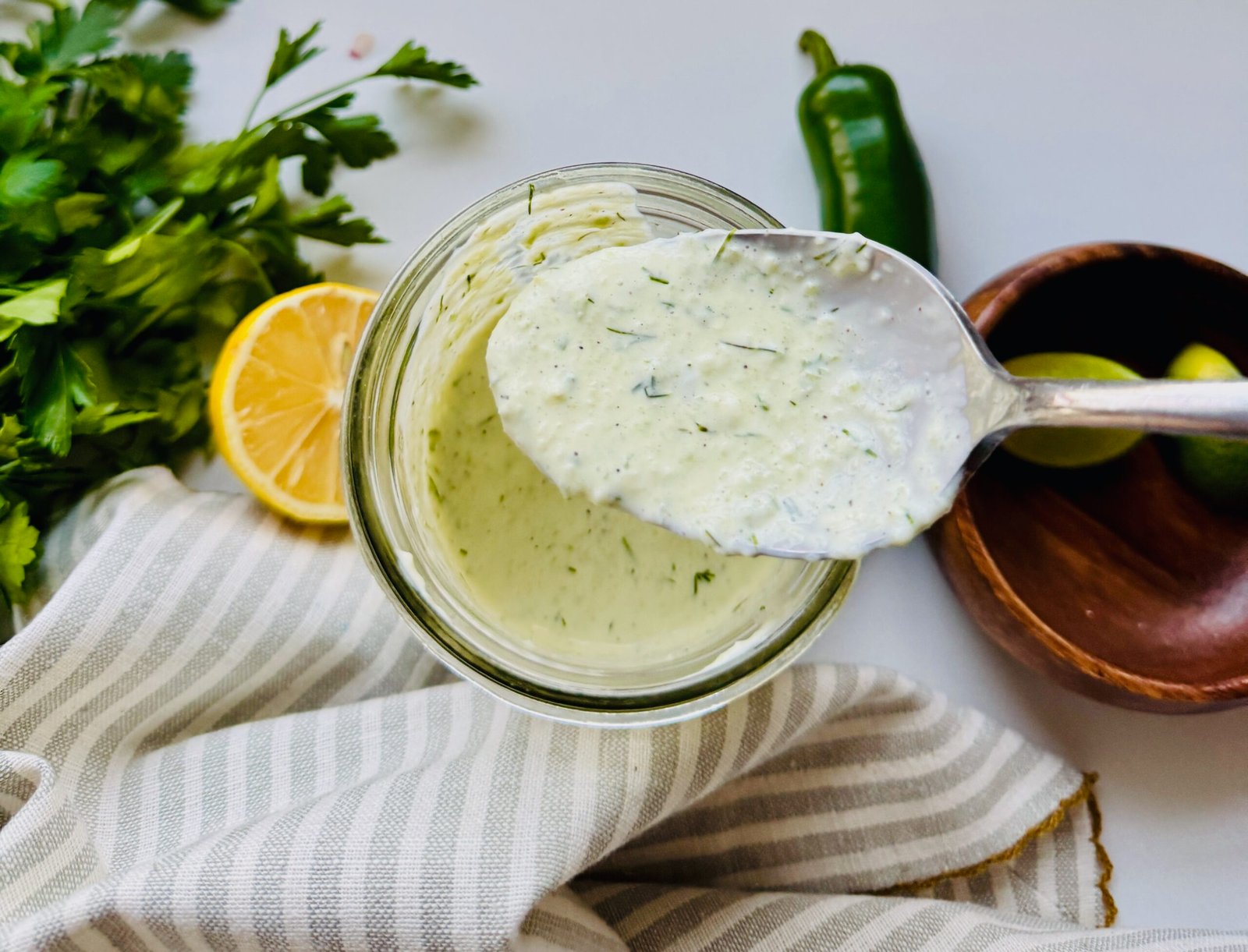 Spoon lifting creamy Greek yogurt sauce from a glass jar with visible herbs