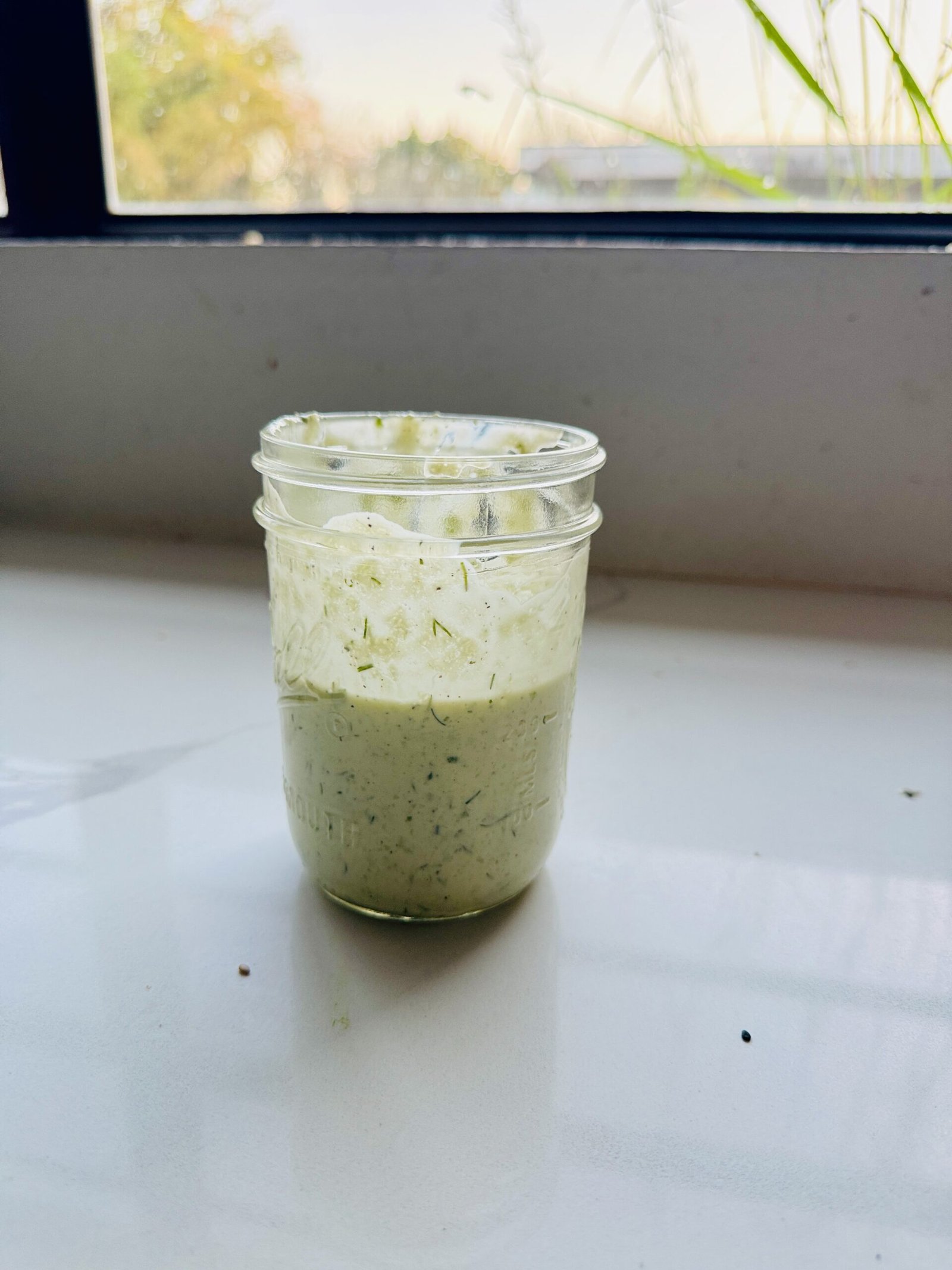 Glass jar of creamy Greek sauce on a kitchen counter near a window with natural light