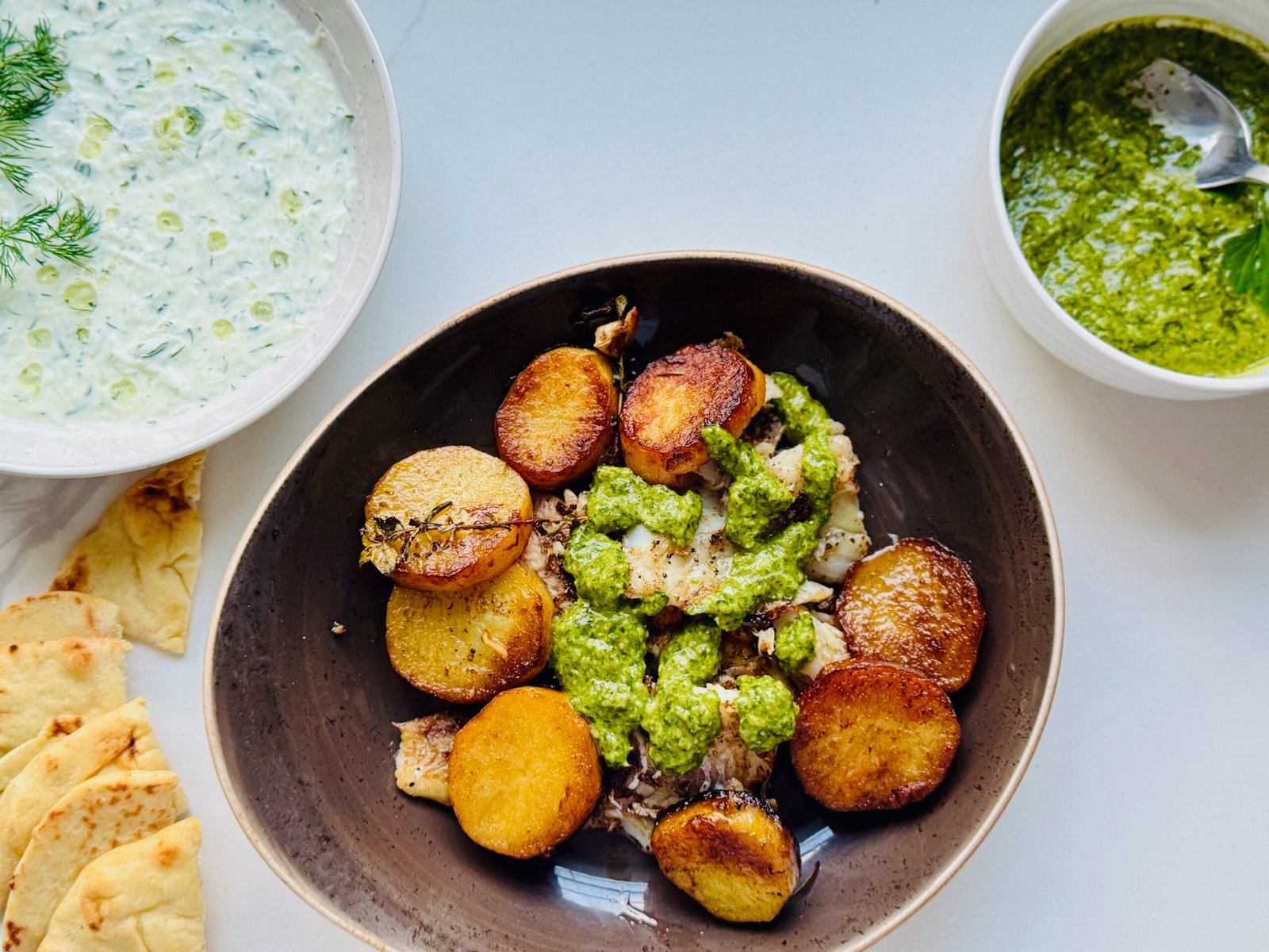 Thin cut melting potatoes served on a plate with green sauce and fish