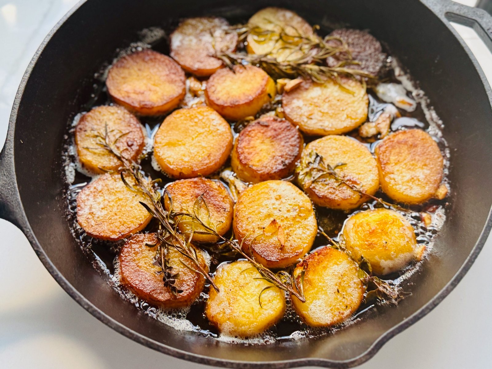 Thin cut melting potatoes in a skillet with golden edges and herbs