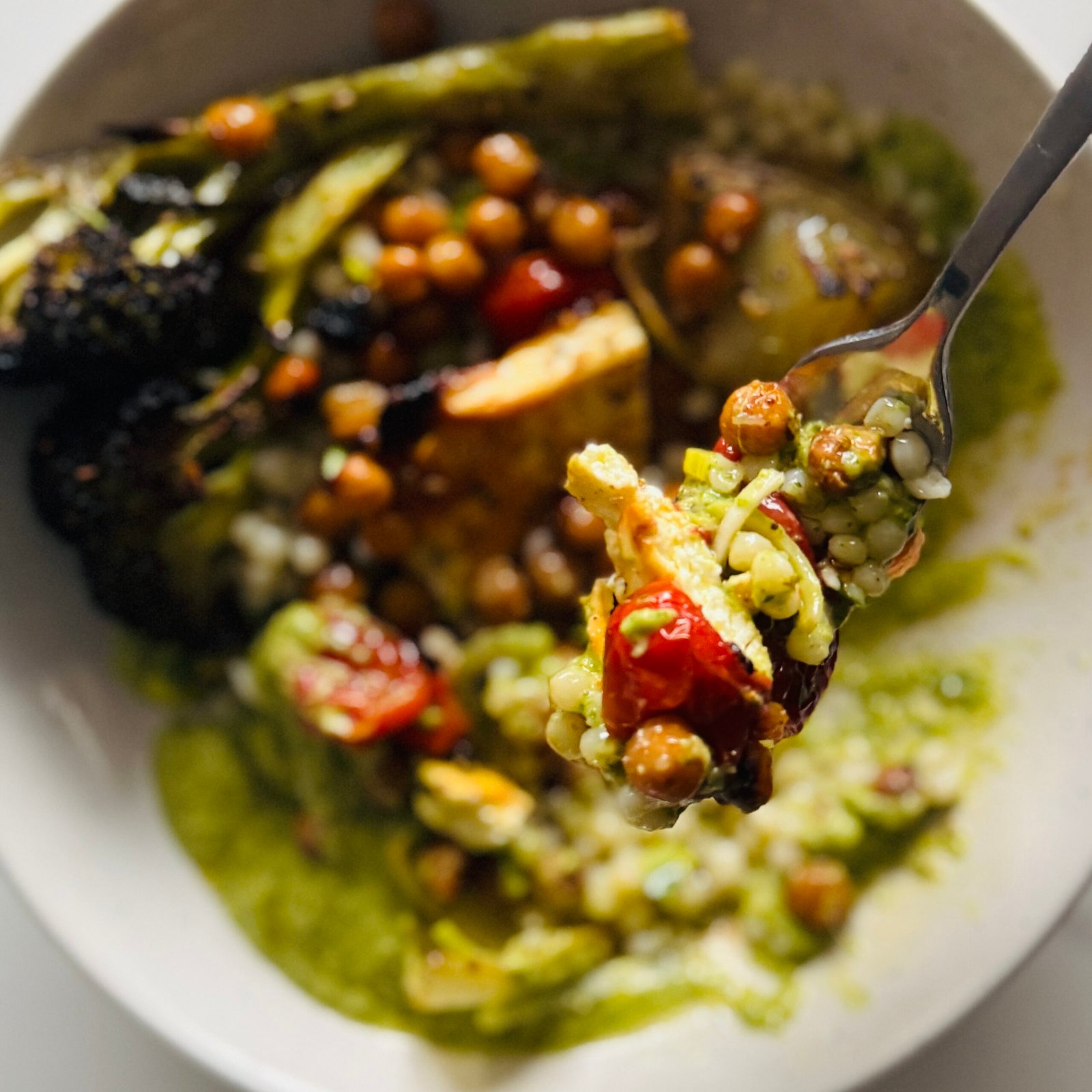 spoonful of green sauce over baked feta chickpea bowl with lime herb couscous