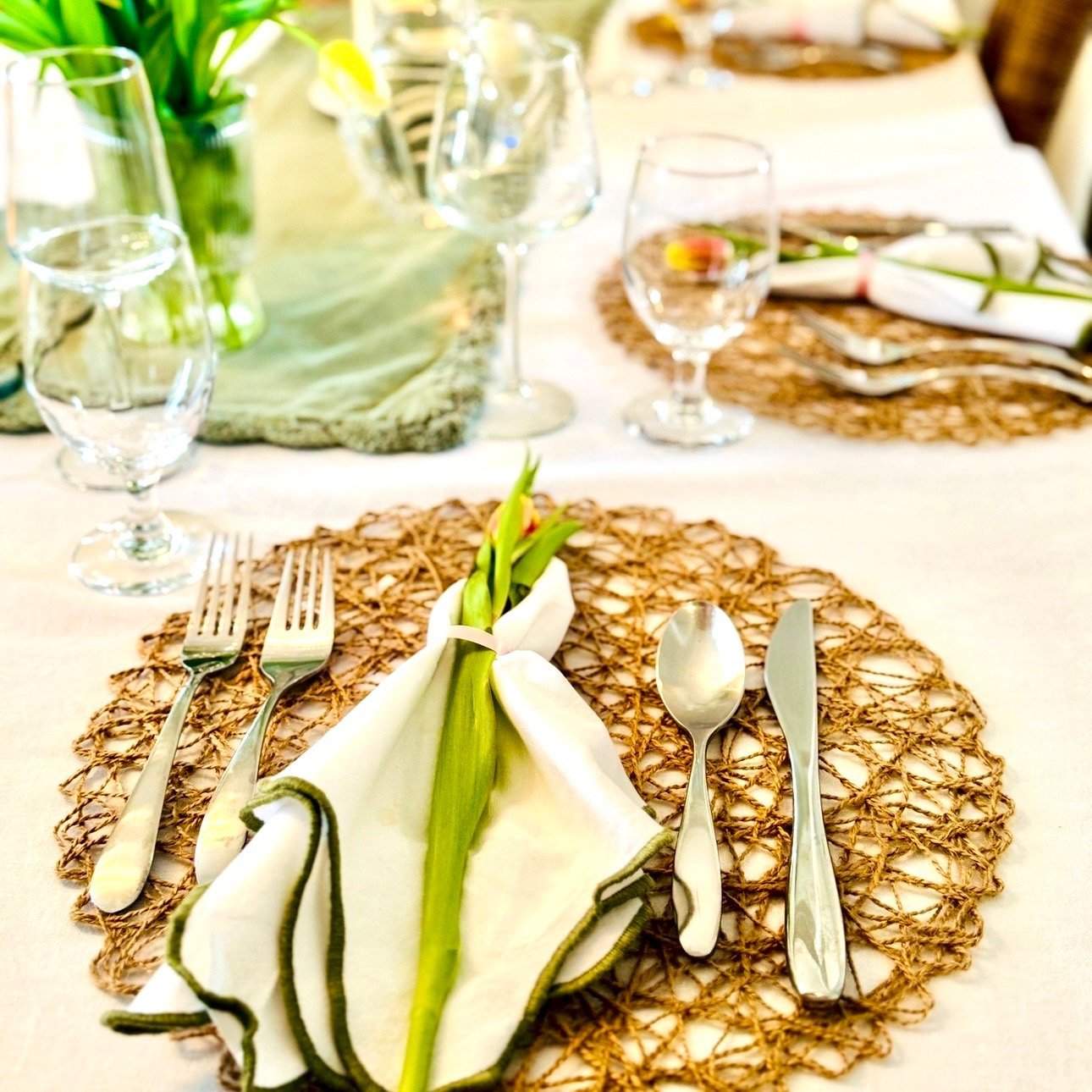 Spring 7 course dinner party table with white linens, green runner, woven placemats, and fresh tulips