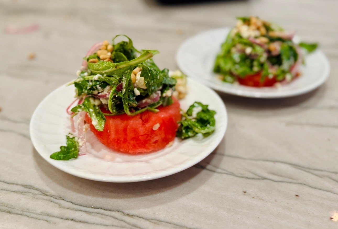 Watermelon salad topped with arugula, feta, red onion, and pine nuts