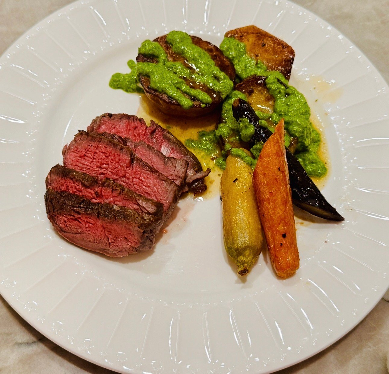 Filet served with melting potatoes, green sauce, and roasted carrots on a white plate