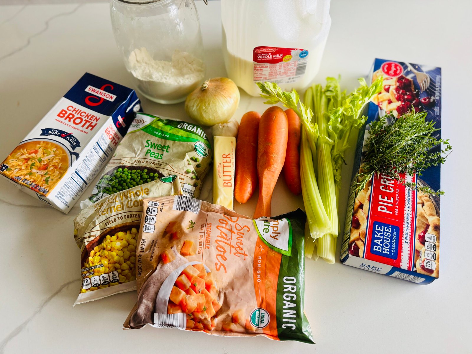 Easy vegetable pot pie ingredients with frozen sweet potatoes, corn, peas, carrots, celery, onion, herbs, milk, chicken stock, butter, flour, and pie crust