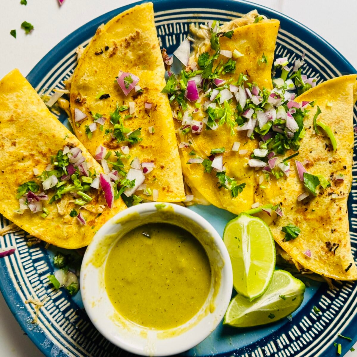 Crispy mojo chicken tacos with melted cheese, onion, cilantro, lime, and tomatillo salsa for dipping
