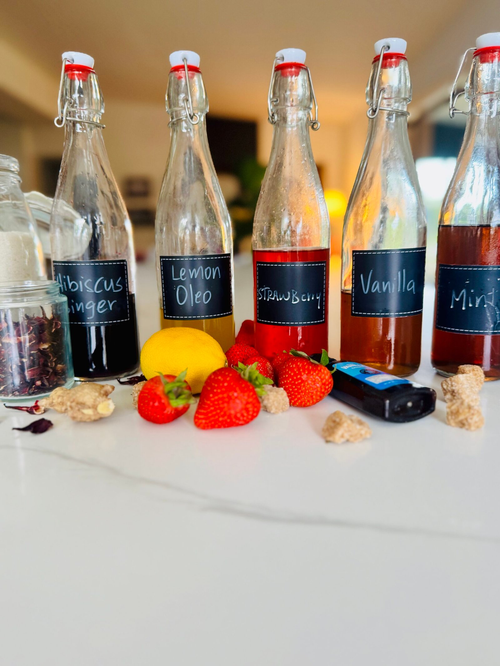 Five homemade drink syrups with mint vanilla lemon strawberry hibiscus and ginger ingredients
