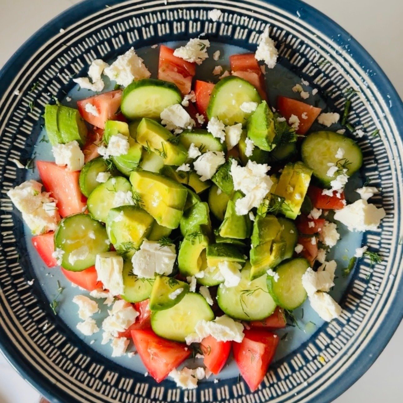 Finished cucumber tomato avocado feta salad topped with crumbled feta and fresh dill.