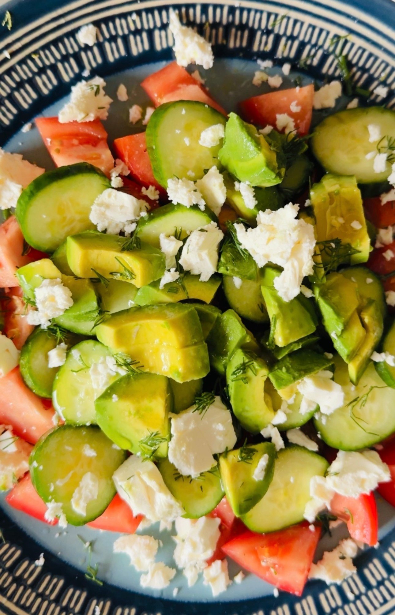 Close-up of cucumber tomato avocado feta salad with fresh dill and crumbled feta.