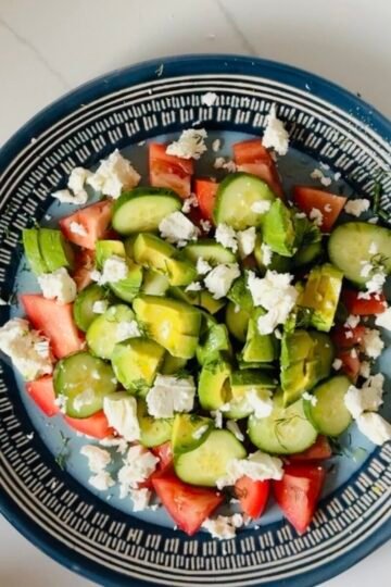 Finished cucumber tomato avocado feta salad with fresh dill and crumbled feta.