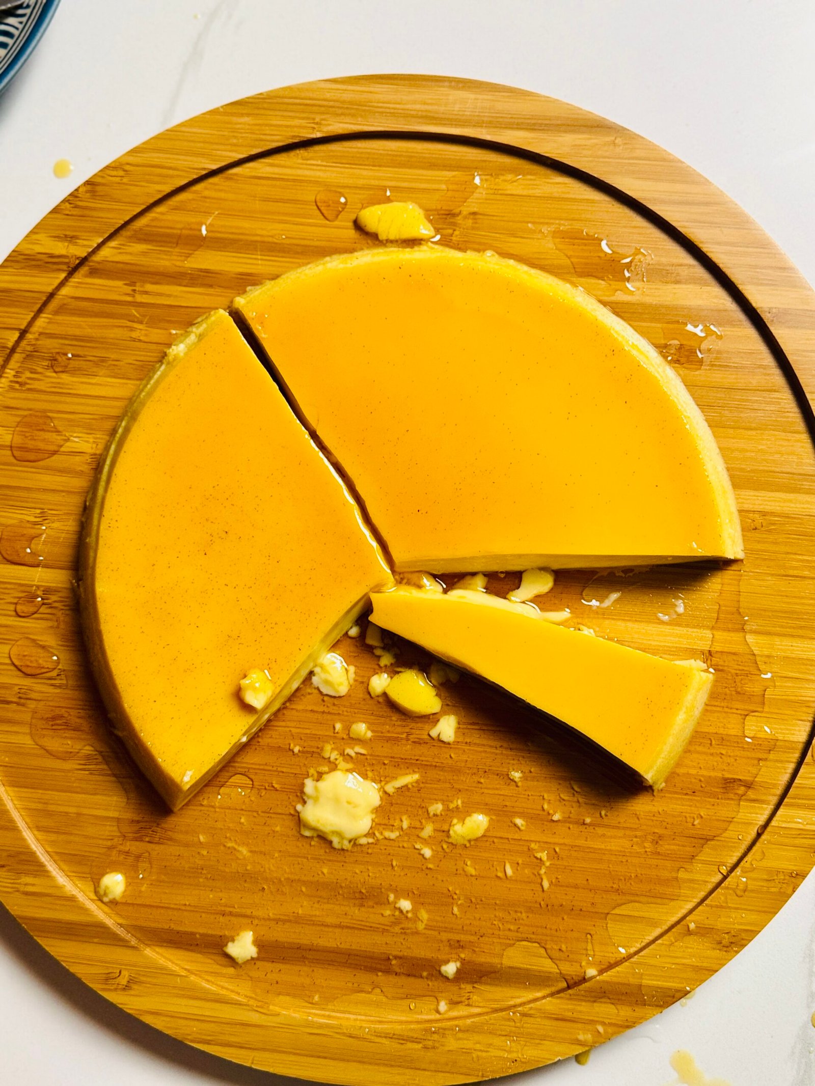 Extra creamy caramel flan on a wooden serving board with a wedge removed.