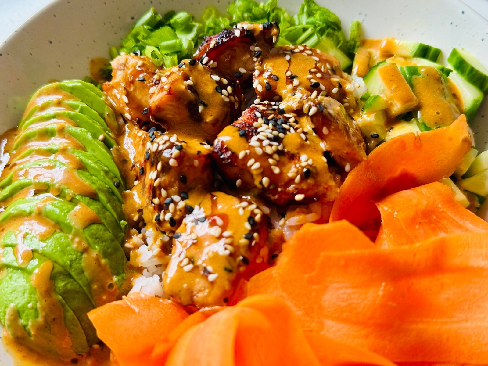 Air fryer soy ginger salmon bites glazed and arranged over rice with cucumber, carrots, avocado, scallions, and sesame gochujang sauce