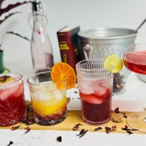 Four hibiscus-ginger drinks: a red Paloma, layered orange spritz, lime soda, and Champagne cocktail.