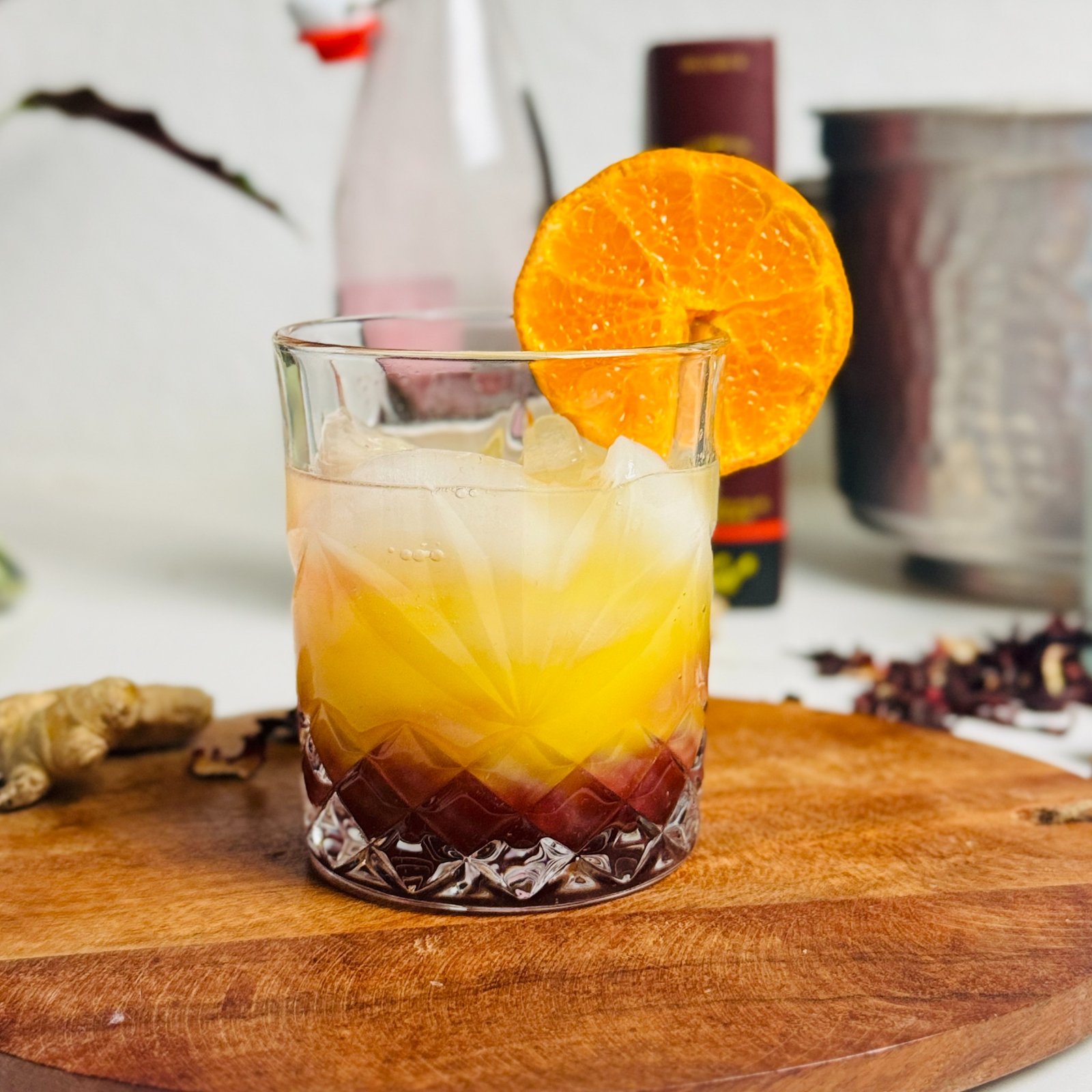 Hibiscus-orange sunrise spritz with dark red and orange layers, ice, and an orange wheel.
