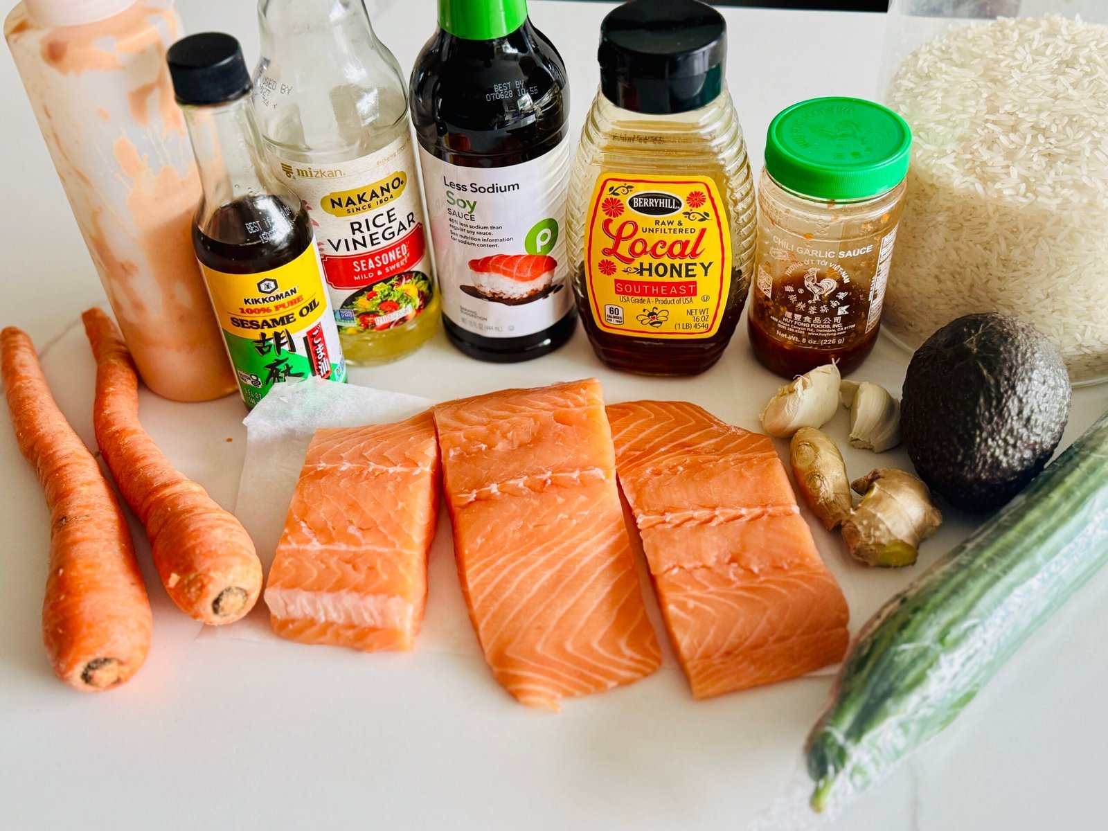 Ingredients for soy ginger salmon rice bowls including salmon, jasmine rice, cucumber, carrots, avocado, scallions, sesame seeds, and gochujang sauce