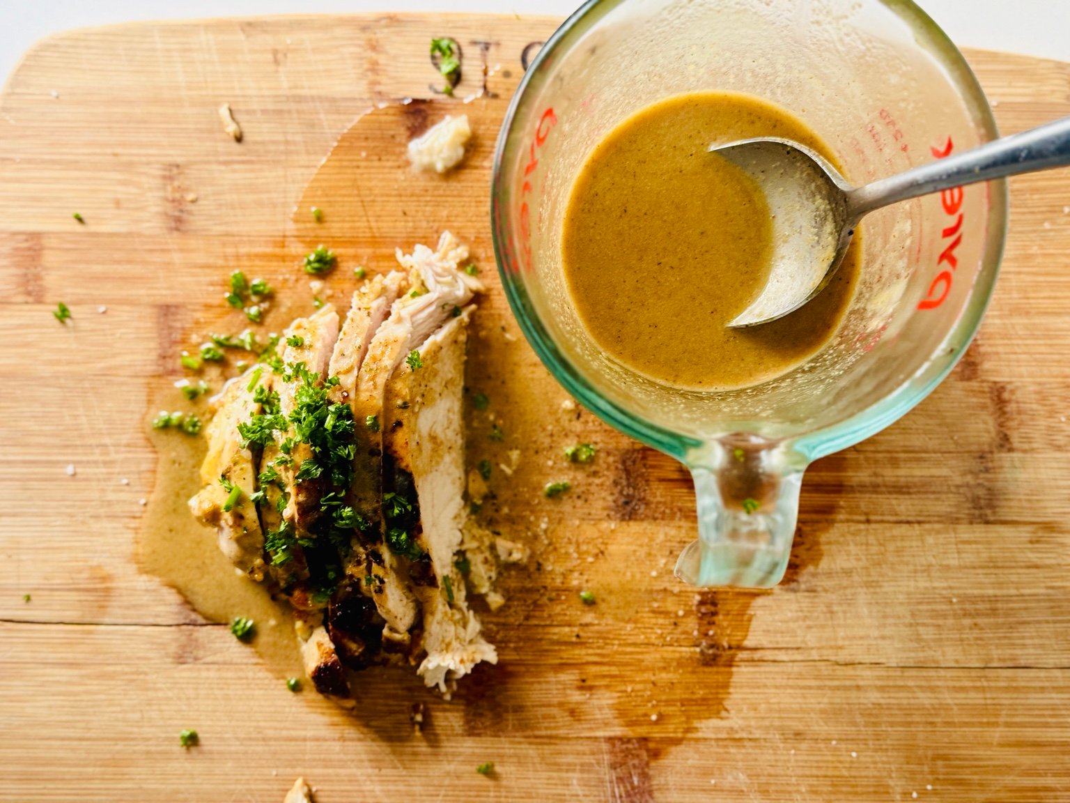 Sliced Lemon Dijon Chicken and Pan Sauce Sliced chicken topped with parsley beside a glass measuring cup of lemon Dijon pan sauce.