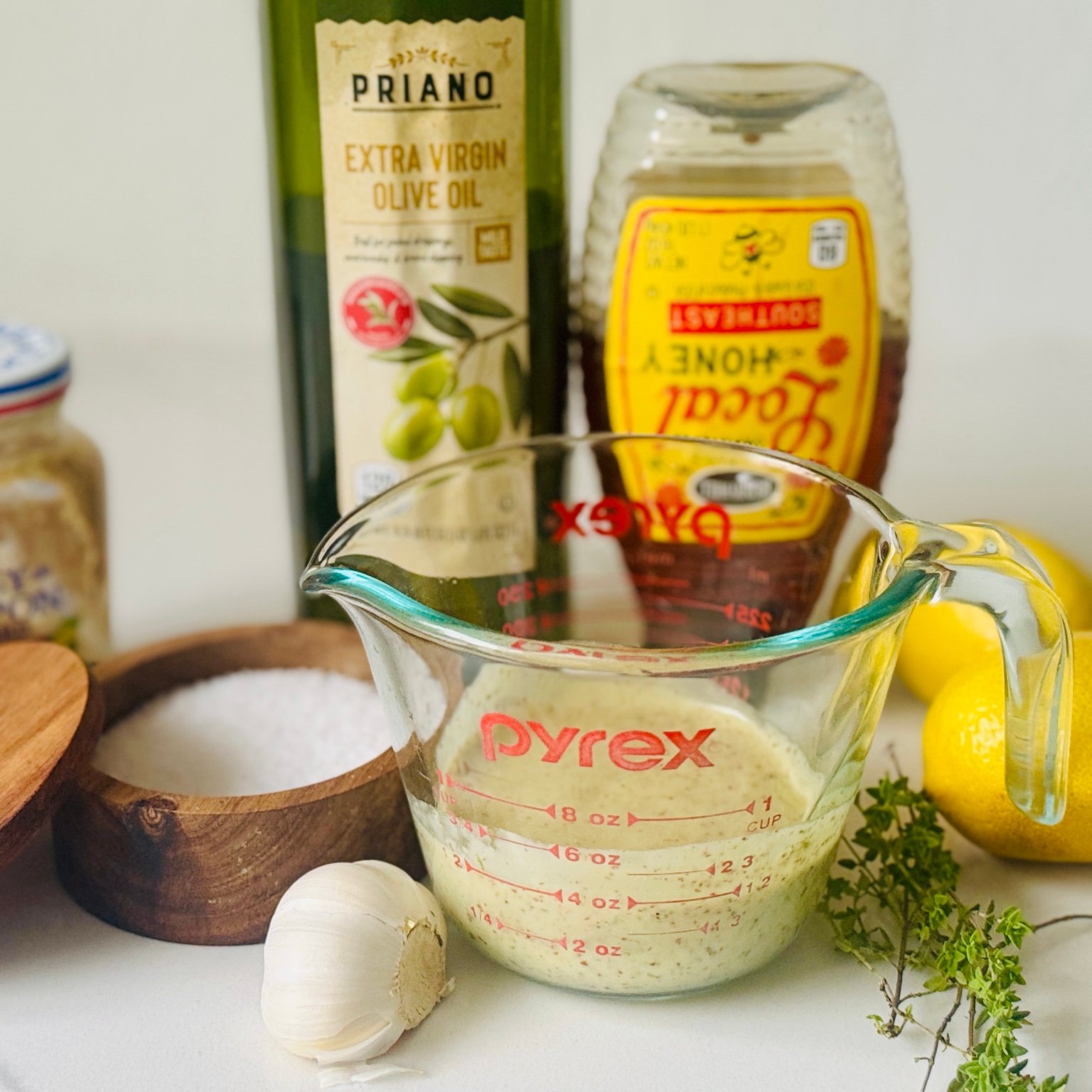Lemon Dijon Marinade in a Measuring Cup Lemon Dijon marinade in a glass measuring cup beside garlic, lemon, herbs, olive oil, and honey.
