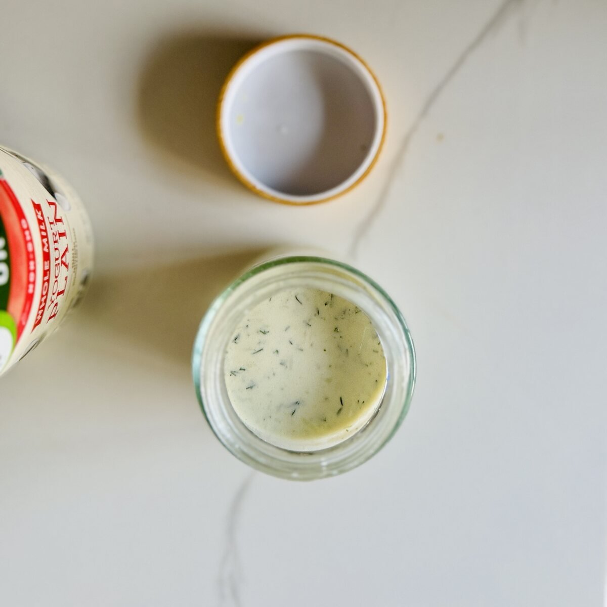 Overhead view of Greek yogurt chicken marinade beside plain Greek yogurt on a light counter
