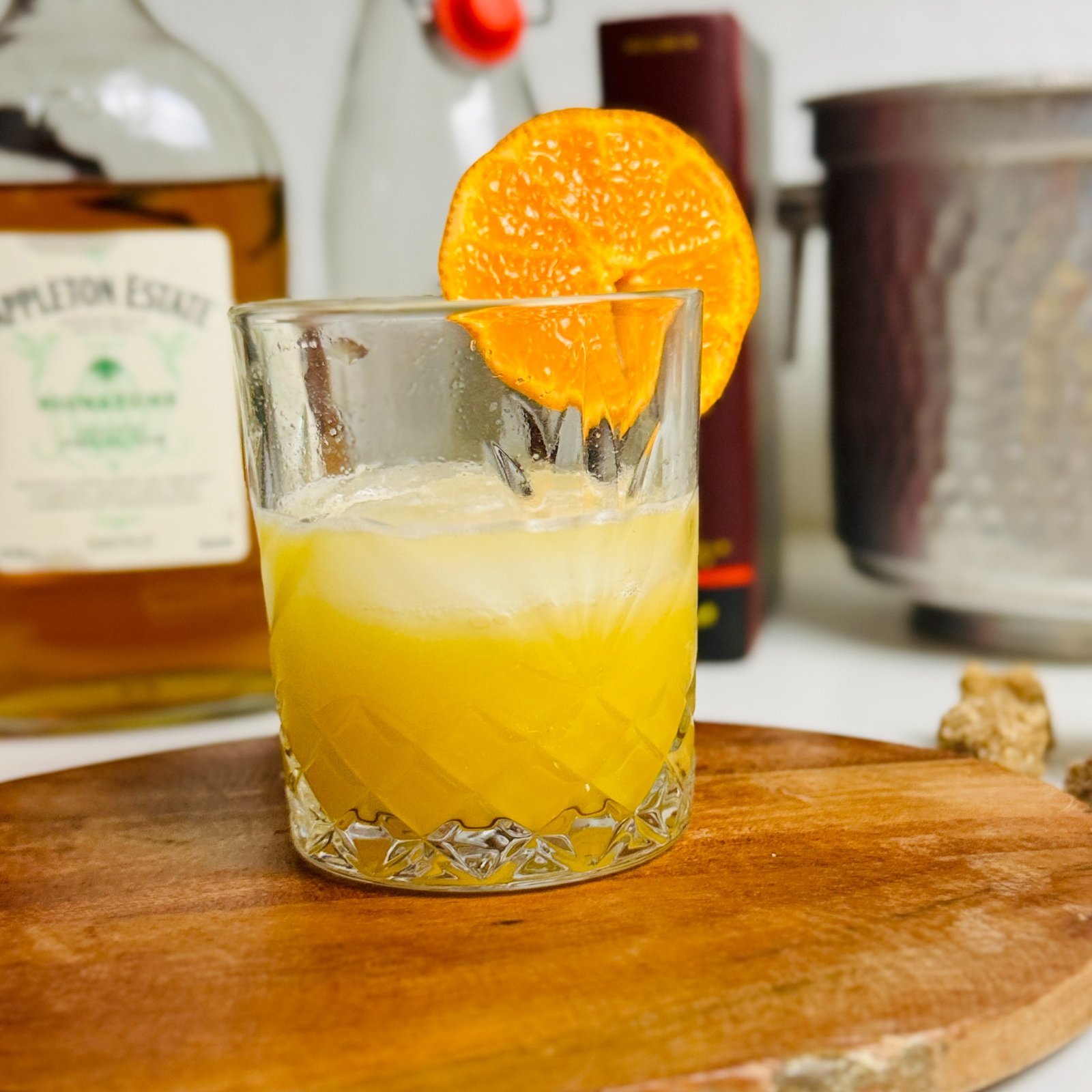 Golden lemon oleo rum punch over ice in a rocks glass with an orange wheel.