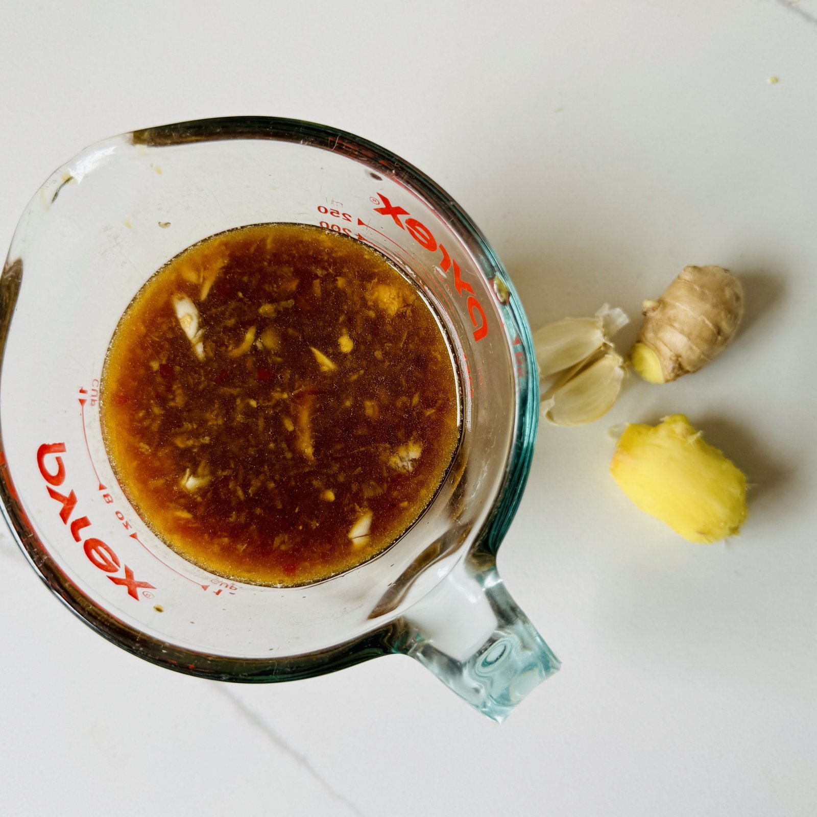 Overhead view of soy ginger marinade in a glass measuring cup with fresh ginger and garlic