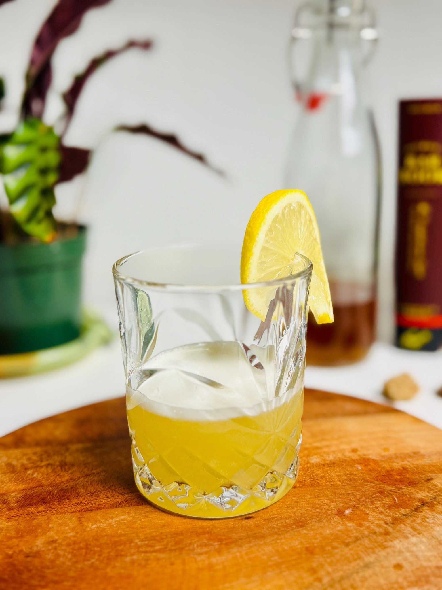 Yellow pineapple-vanilla vodka sour over ice in a rocks glass with a lemon wheel.