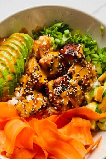 Soy ginger glazed salmon rice bowl with jasmine rice, cucumber, carrot ribbons, avocado, scallions, sesame seeds, and creamy gochujang sauce