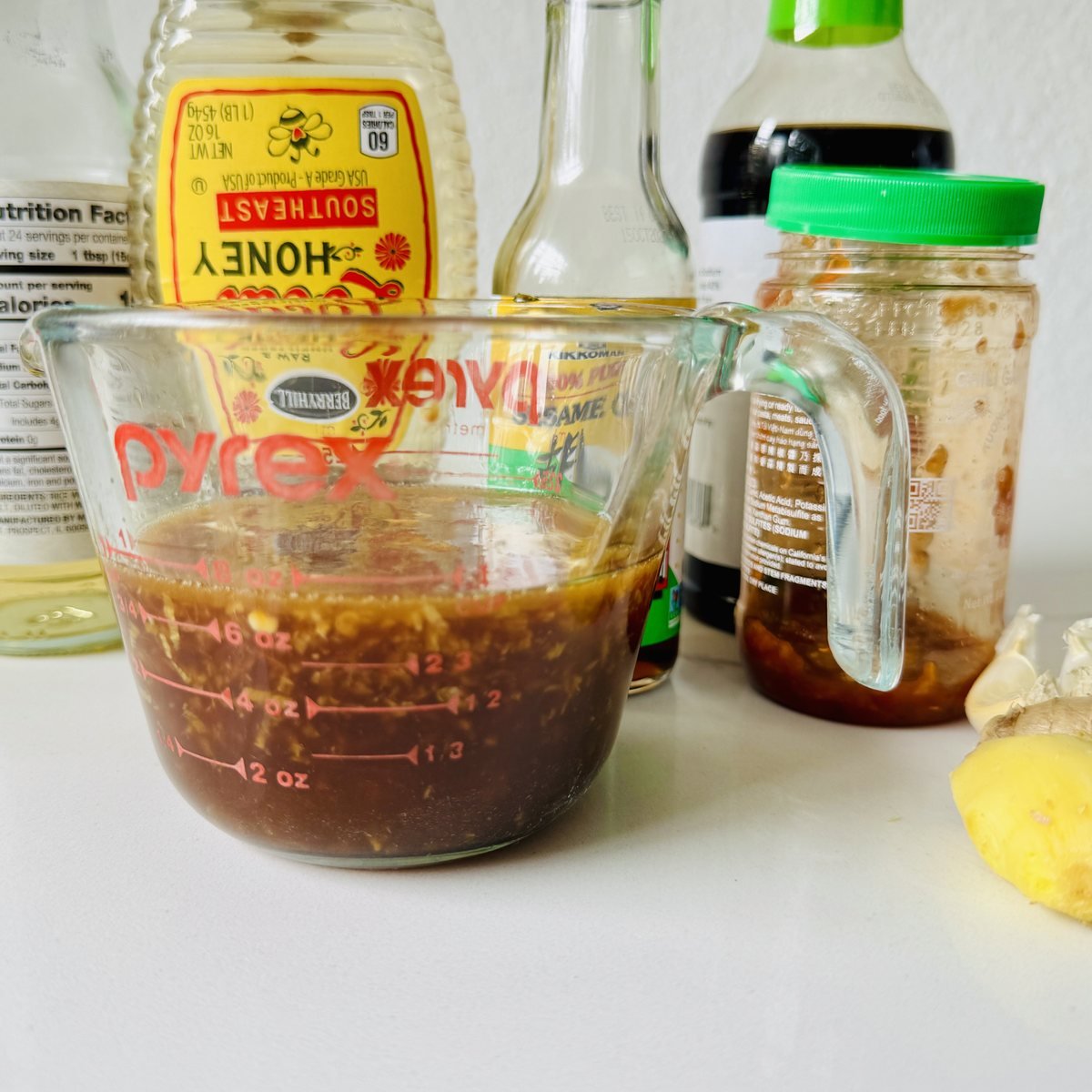 Soy-ginger marinade in a measuring cup surrounded by soy sauce, honey, sesame oil, rice vinegar, ginger and garlic.