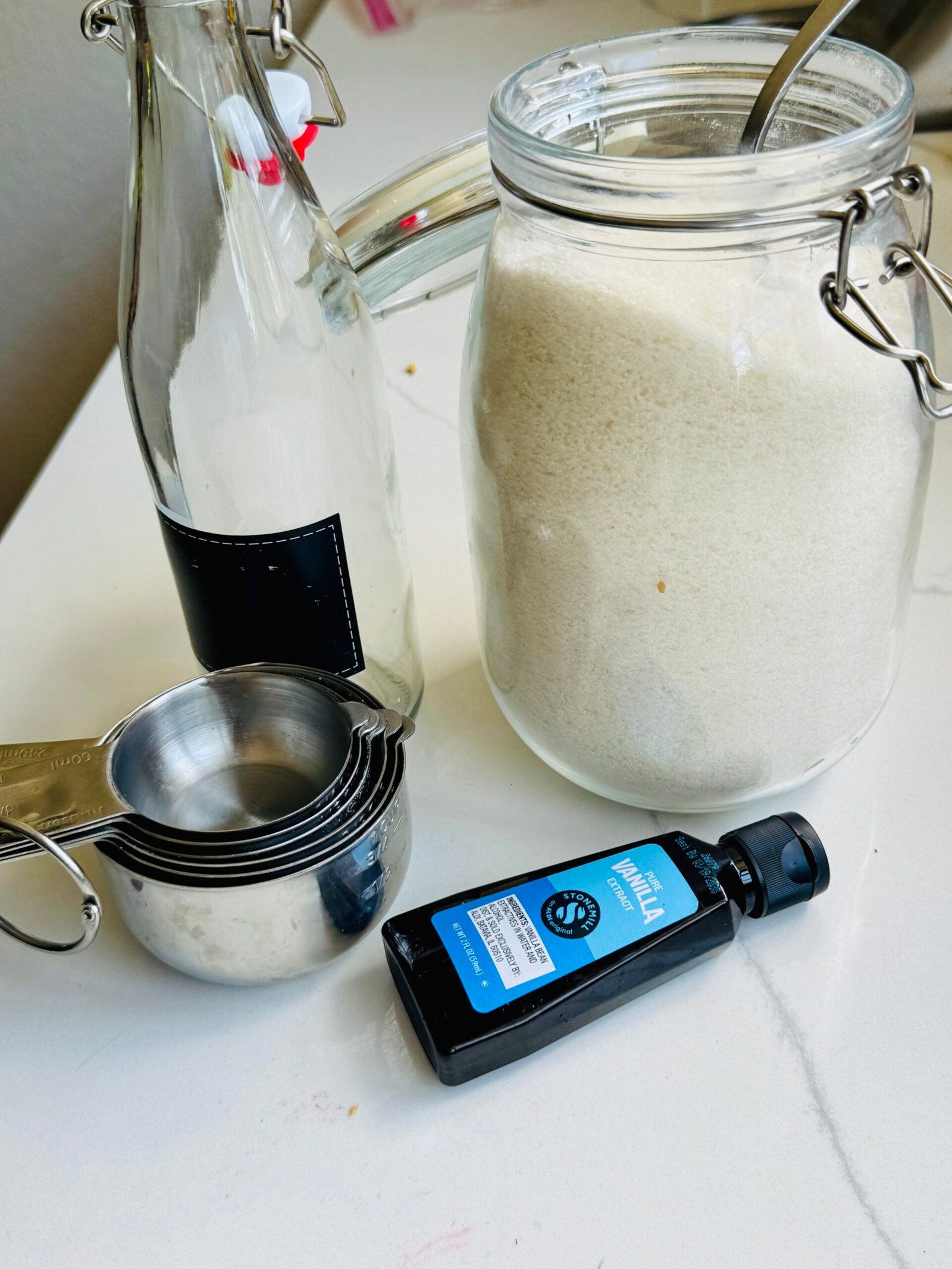Granulated sugar, vanilla extract, measuring cups, and a glass bottle for homemade vanilla syrup.