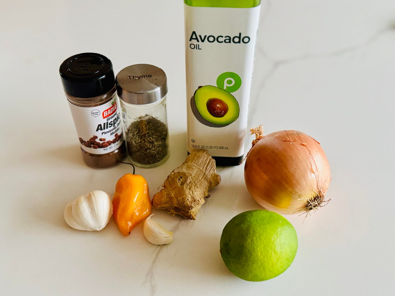 Fresh jerk marinade ingredients including allspice, dried thyme, garlic, ginger, green chili, onion, lime and oil.