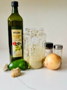 Blended jerk marinade in a clear blender jar beside olive oil, onion, green pepper, ginger, garlic and dried spices.
