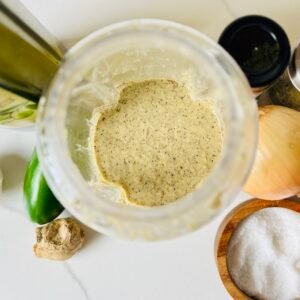 Overhead view of freshly blended jerk marinade with visible flecks of allspice and herbs in a blender jar.