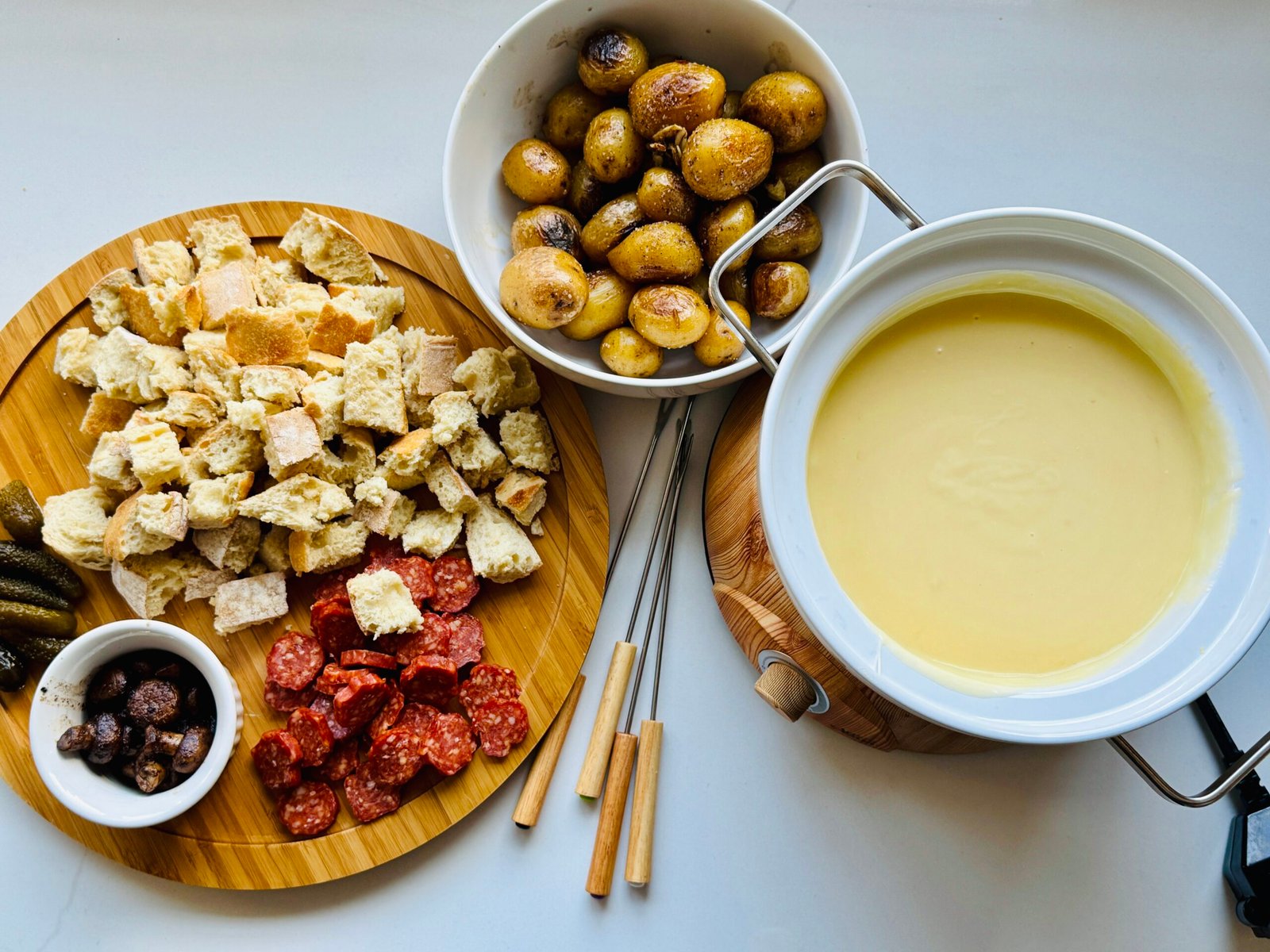Fondue meal with warm melted cheese, bread, and dipping foods arranged around the pot.