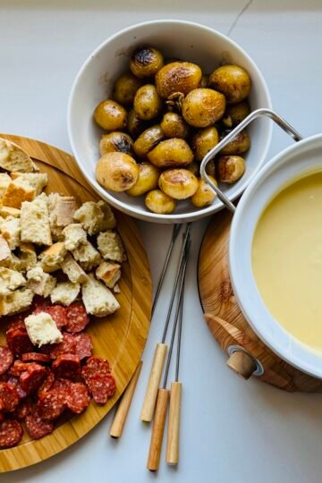 Gruyère and Gouda fondue served with a variety of foods arranged for dipping.