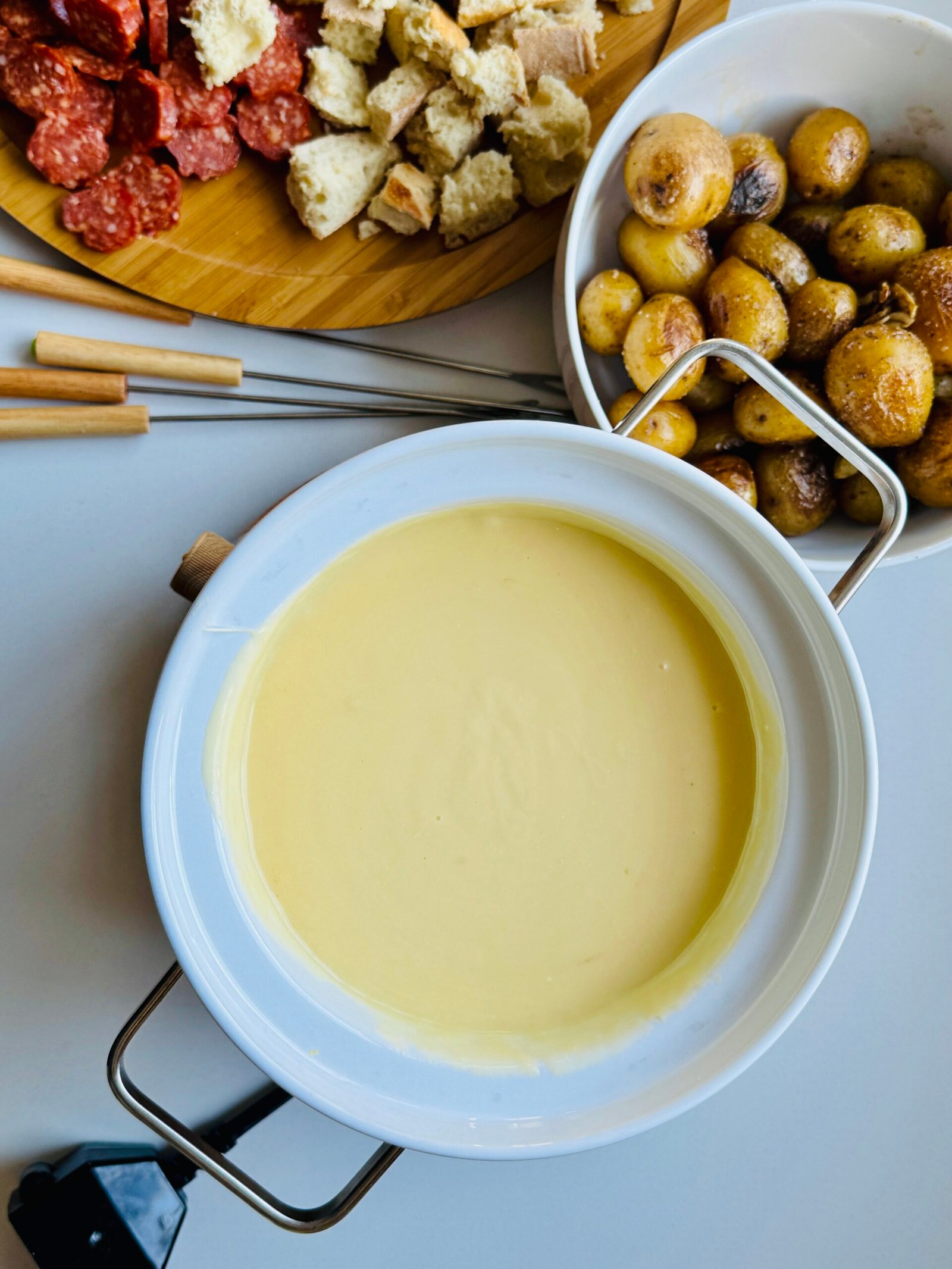 A warm pot of melted Gruyère and Gouda cheese with accompanying foods for dipping.