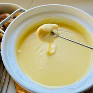 Close-up of smooth melted cheese fondue in a white pot with a fondue fork.