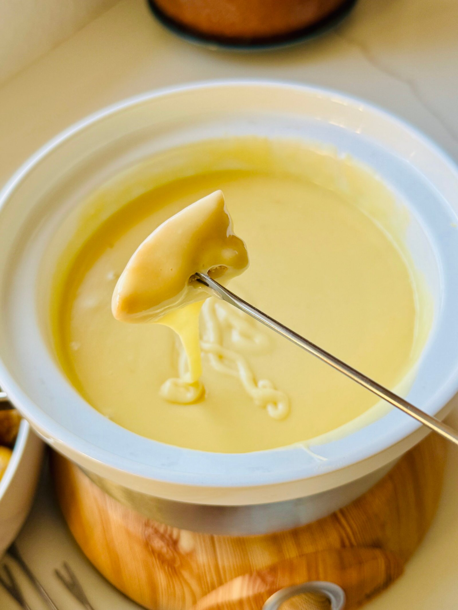 A bite lifted from creamy Gruyère and Gouda fondue on a fondue fork.